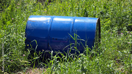 Environmental threat from an abandoned blue metal drum resting in wild grass