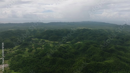Rolling hills covered with tropical vegetation and scattered villages under cloudy sky. Siargao, Philippines.