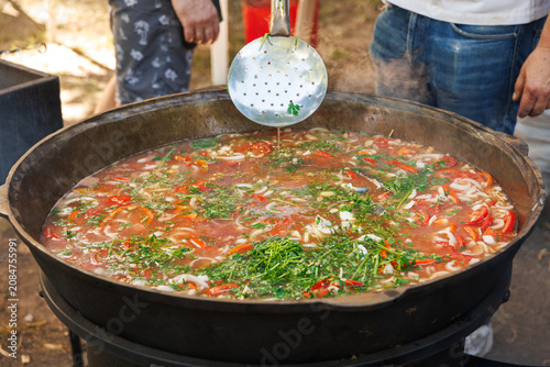 Traditional fish soup with fresh tomatoes being cooked outdoors at a vibrant culinary food festival