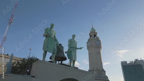 Statues stand in front of clock tower in Buenos Aires at sunset time