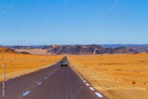 A straight asphalt road near Djanet. The Tadrart Rouge mountains in the background. Djanet, Algeria, Africa