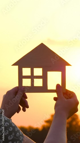 Woman holds wooden house model against glowing sunset, symbolizing dream home, home ownership and future plans. Vertical video captures hope, stability and new beginnings.