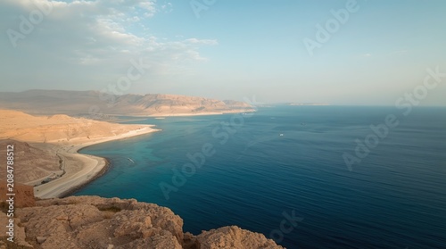 Panoramic view of the Dead Sea from a high vantage point showcasing its striking blue waters and surrounding arid landscape with distant mountains under a partly cloudy sky