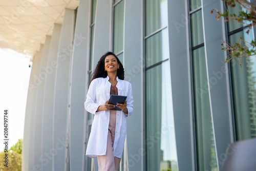 Young woman in a lab coat walking confidently, holding a digital tablet