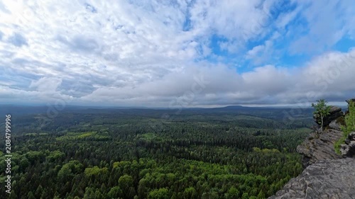 Dramatic morning view from Grosser Zschirnstein, Saxon Switzerland, Germany, with distant horizon, layered clouds, deep forest below and sandstone rocks in foreground.