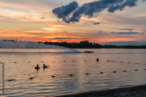 A sandy beach at a state park at sunset with silhouettes of 2 or 3 swimmers in the distance in upstate New York.