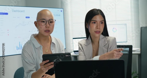 Asian female coworkers using a tablet and computer to review financial datum and results. Teamwork and technology integration for successful investment and data research.