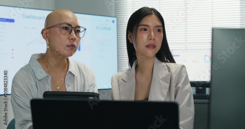 Asian female colleagues working together on a computer monitor. Analysis of financial information and investment strategy during a professional corporate briefing.