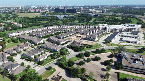 Vue Las Colinas neighborhood homes cluster beside undeveloped land tracts. Compact geometric roofing dominates view as shadows stretch across lawns within peaceful residential zone in Irving TX