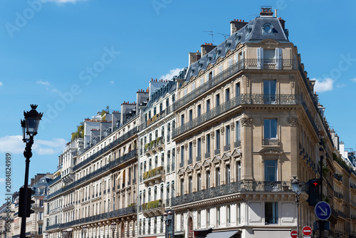 Magnificent Haussmann-style apartment buildings line the Avenue de l'Opera in the 2nd district of Paris, under a vivid blue sky.