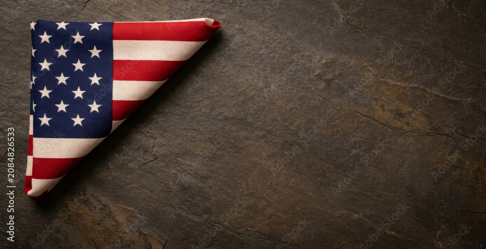Obraz premium A folded American flag rests against a textured stone background, symbolizing patriotism and national pride in a minimalist composition.