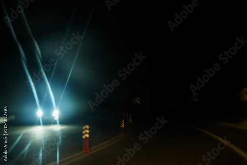 Obraz na plátně Blinding car headlights on a dark night road bend with reflective traffic markers