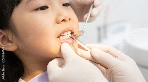 Asian child receiving fluoride varnish application from dentist during pediatric dental treatment, close-up of teeth, dental mirror and brush in clinic
