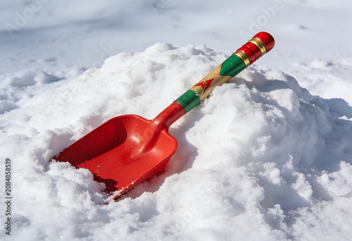 Red snow shovel with colorful handle stuck in a pile of snow outdoors