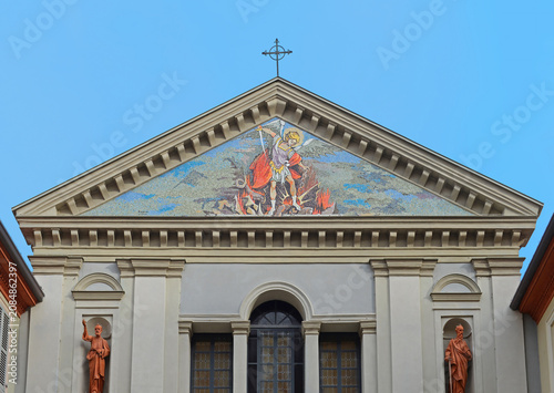 Top gable of Saint Michaels church (San Michele Arcangelo) with colourful mosaic of the archangel beating the dragon or devil in Tortona, Italy with blue sky