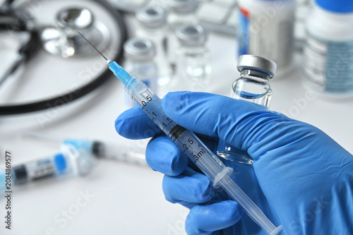 Medical personnel holding syringe needle with generic vaccine booster and vial