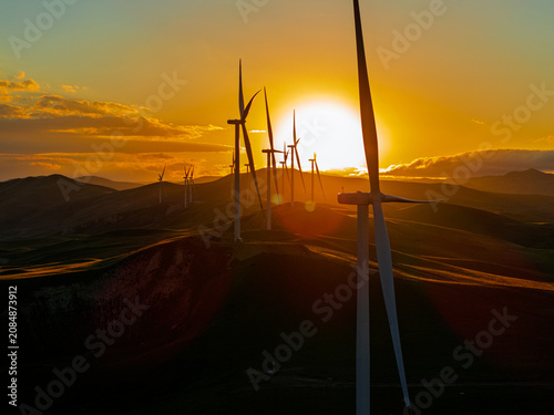 Beautiful sunset field with wind mill generators. Windmill silhouette on mountain at sunset