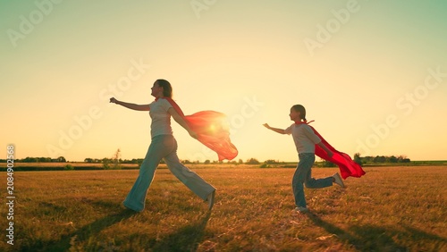 Konstfotografi Happy children playing superheroes, running sunny field in red capes