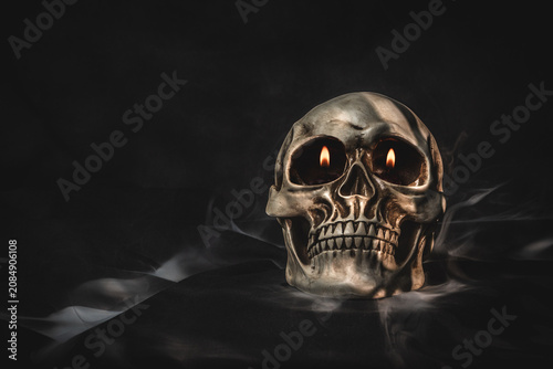 Human skull with glowing eyes surrounded by mysterious smoke on dark background