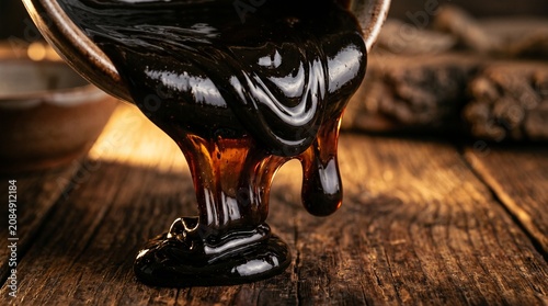 Thick dark syrup pouring onto rustic wood, glossy molasses texture, warm amber highlights, artisan food styling, sweet indulgent topping.