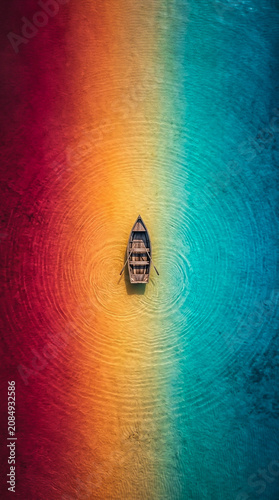 Minimalist wooden canoe floating in the center of rainbow colored tropical sea surface