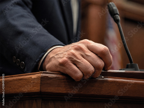Close up of a witness testifying on the stand in federal court with hand resting on polished wood beside a microphone during formal legal proceedings and courtroom testimony before a judge