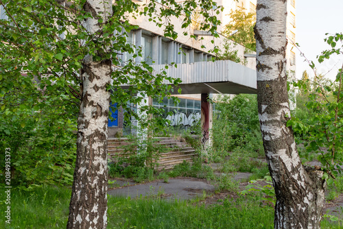 Abandoned concrete building overgrown with green trees and wild in the city