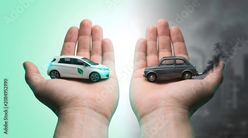 Concept of comparing eco-friendly electric car and polluting combustion vehicle held in human hands to illustrate climate change with environment