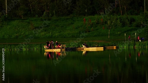 Adults and children enjoy recreational fishing from a lakeside platform during a beautiful summer sunset in Canada. A peaceful outdoor scene highlighting family leisure, nature, and lakeside recreatio