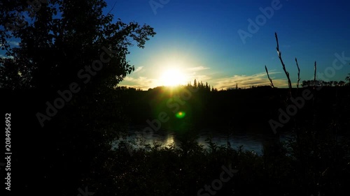 The last rays of a summer sunset illuminate a large Canadian river as the water flows gently through the darkening landscape. Warm golden colors contrast beautifully with the deep blue tones of approa