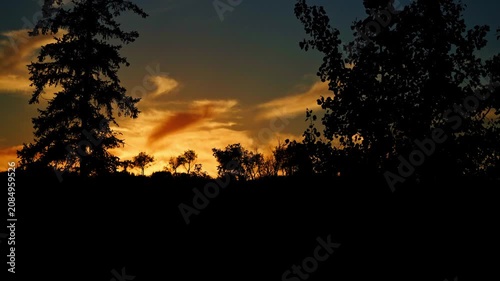 Distant views of spectacular colorful clouds illuminated by the last rays of the setting sun. Rich golden, orange, pink, and deep blue tones create a dramatic summer evening sky.