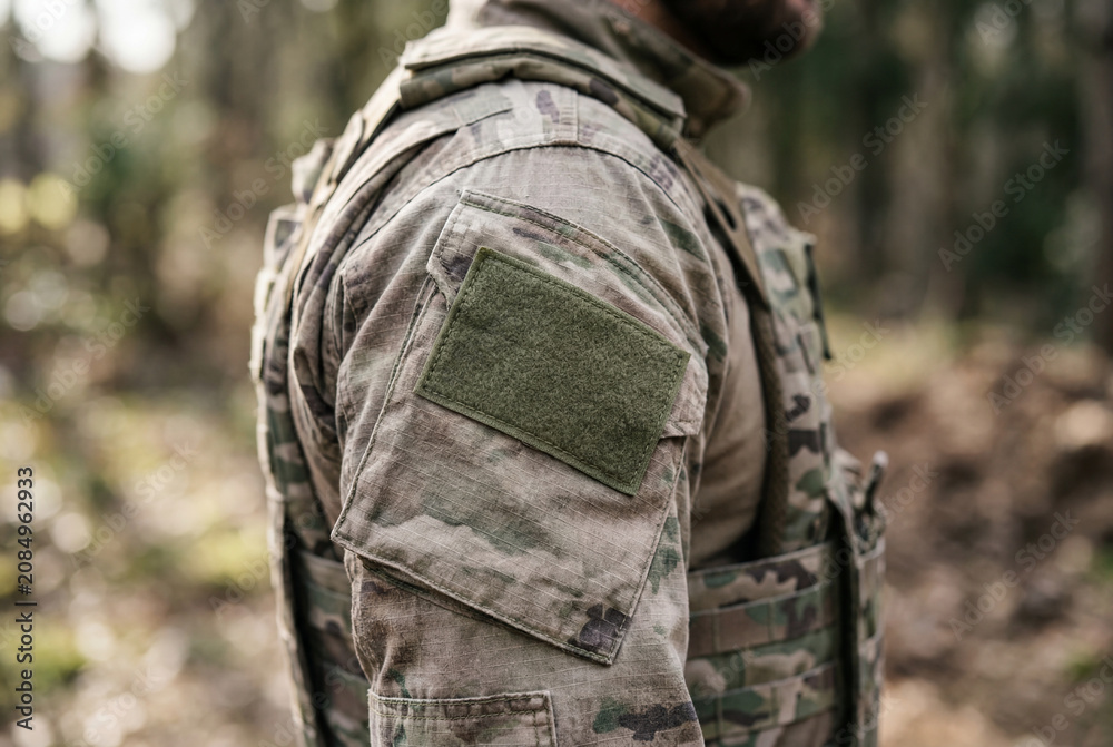 Fototapeta premium Close up of tactical camouflage uniform sleeve with blank velcro patch in forest