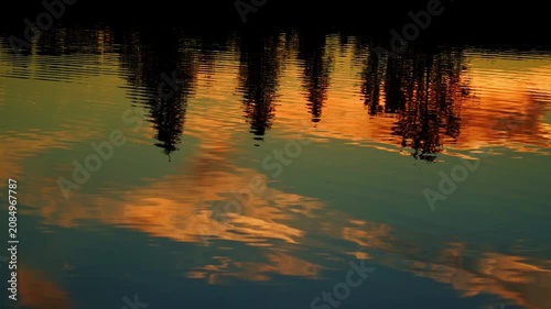 A breathtaking summer sunset reflects across the calm waters of a Canadian lake. Golden, orange, and warm evening colors create a peaceful landscape as the sun slowly disappears below the horizon.