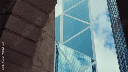 A low-angle view of a bustling urban landscape in Hong Kong, featuring towering modern high-rise buildings with sleek glass facades and prominent skyscrapers
