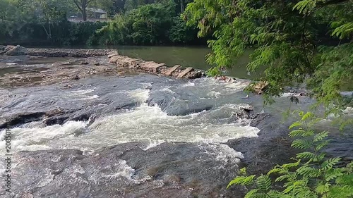 High angle shot of river water cascading over a small rocky dam structure creating white foam and rapids