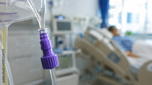 Enteral feeding tube, purple connector, clear plastic, hospital room, patient bed, medical equipment close up with blurred background for clinical care detail