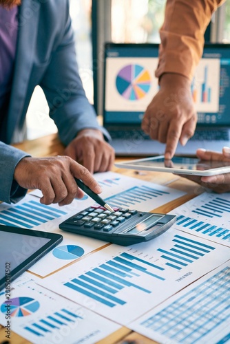 Business team reviewing accounting financial reports with calculator, charts, tablet, and dashboard on laptop during office meeting, supporting budget analysis, financial planning, and reporting workf