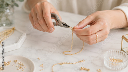 Hands of a female artisan assembling a gold chain necklace using jewelry pliers in a bright and clean studio workspace close up shot
