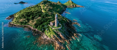 Aerial view of lighthouse on rocky island surrounded by turquoise ocean water