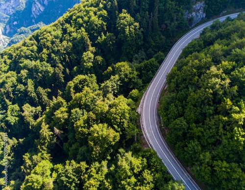 Drone view of a curved mountain road surrounded by lush forest, ideal for clean energy, EV, and green transportation concepts.