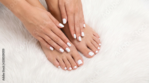 A woman's manicured hands are touching pedicured feet on a white rug.