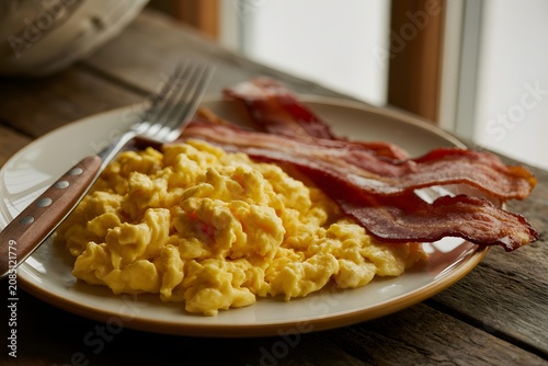 Scrambled eggs with crispy bacon strips on rustic wooden table, breakfast