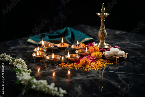 Traditional Diwali oil lamps with marigold flowers on black marble. Brass diya oil lamps for Hindu festival celebration. Spiritual puja setup with burning candles and jasmine.