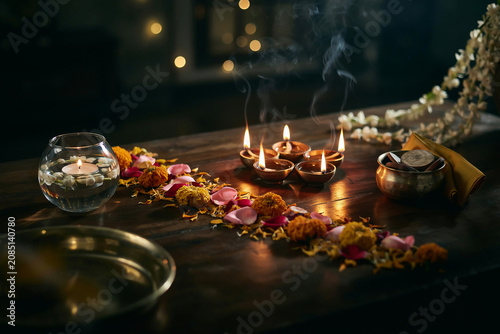 Traditional Diwali oil lamps on wooden table, glowing diya lights with flower petals and incense smoke, festive Indian celebration background