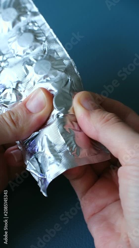 Close up hands pushing small, white, round tablet out of silver foil blister pack, demonstrating process of taking medication for health treatment concepts. Person taking white pill from blister pack