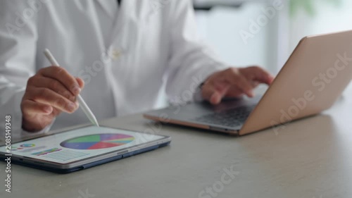 ノートパソコンとタブレットPCを使って作業する白衣の男性。医療、科学、研究、開発、経営、DX、AI