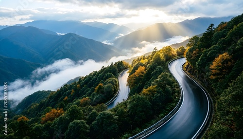 Jalan Berkelok di Pegunungan dengan Cahaya Matahari Menembus Awan dan Kabut Pagi