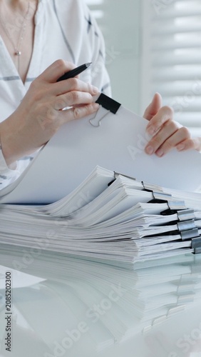 Person's hands meticulously reviewing and organizing extensive business documents and financial reports fastened with binder clips. Illustrating the demanding nature of administrative work