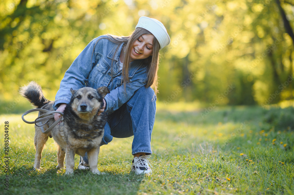 Fototapeta premium Young woman enjoying walk, stroking a dog in park