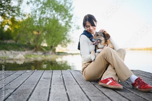 Woman petting happy dog sitting on dock by lake